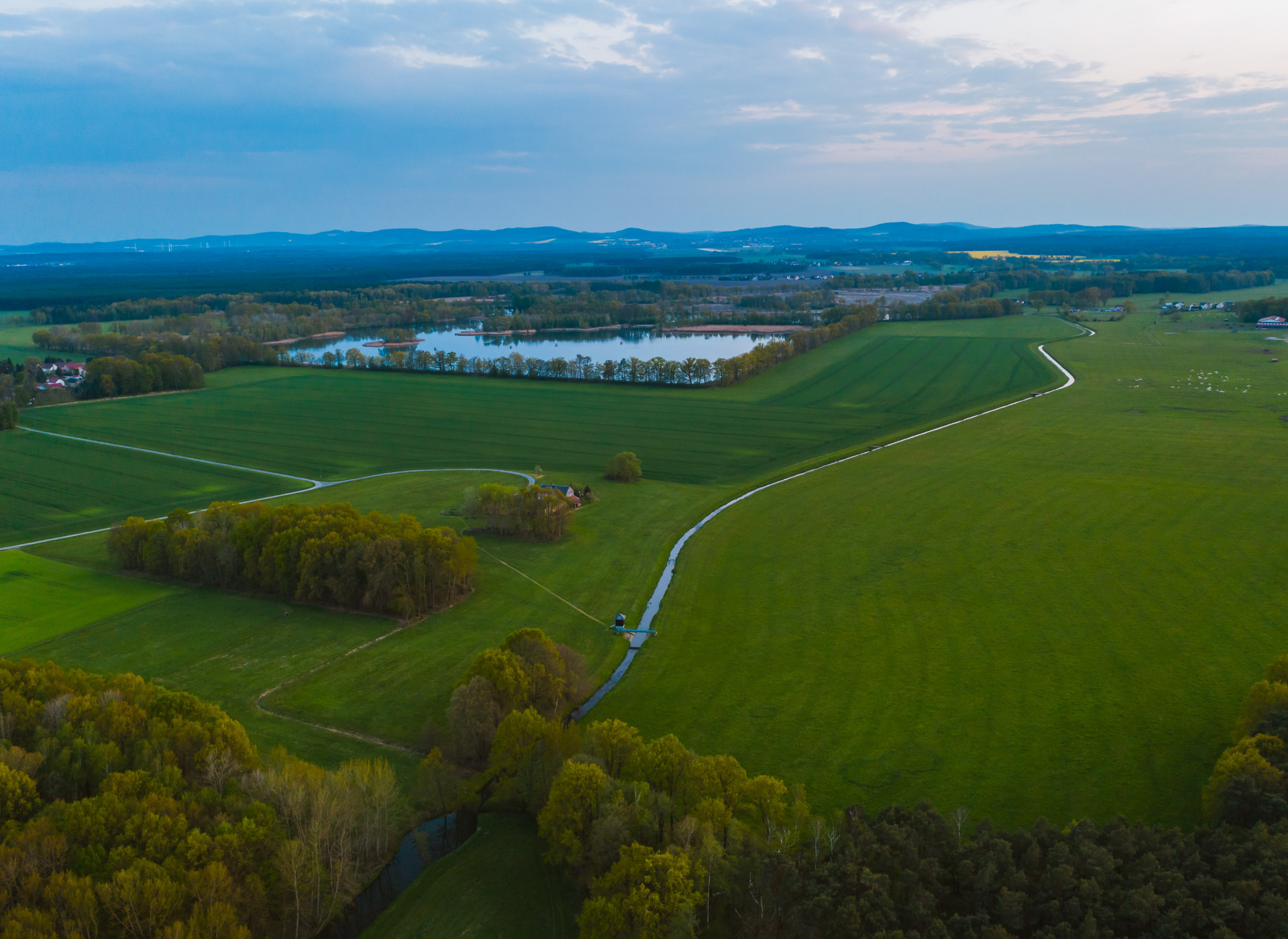 Foto von der Lausitz, grüne Landschaft und ein See, im Hintergrund Berge