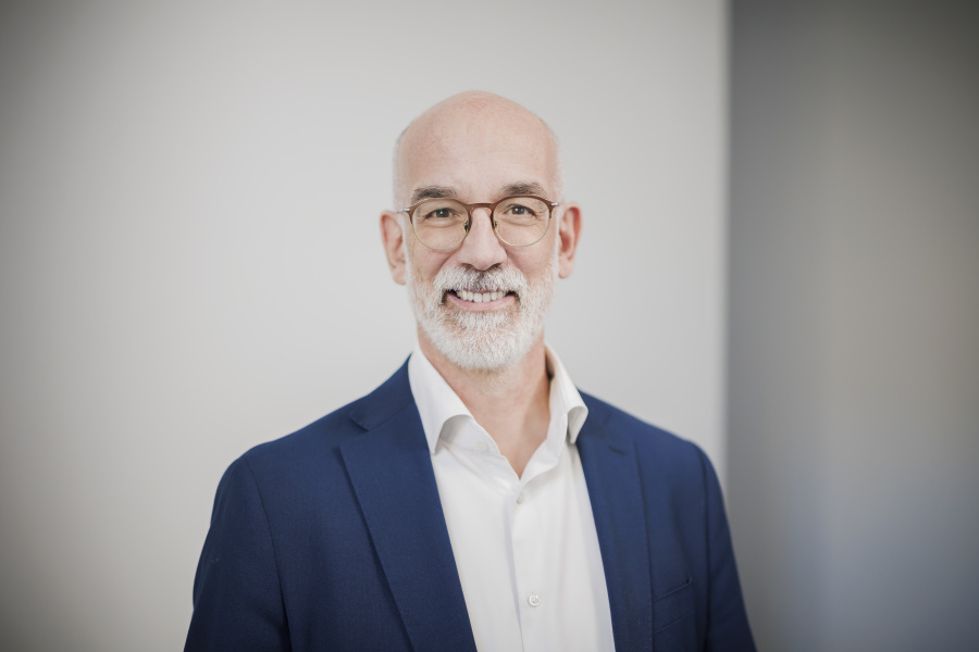 Männlich gelesene Person mit Brille blickt lächelnd in die Kamera.