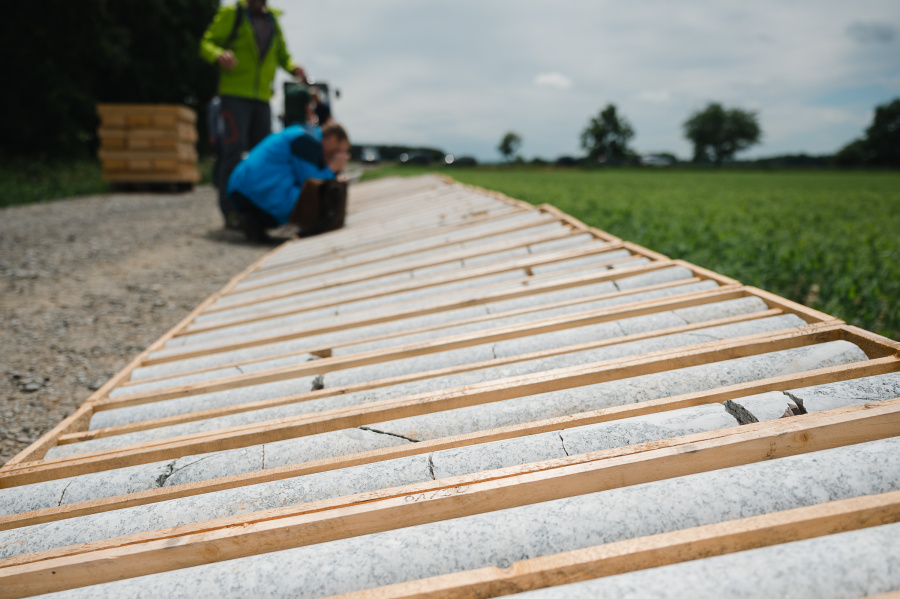 Bohrkerne der Probebohrungen liegen aufgereiht auf dem Boden. Eine Person betrachtet sie prüfend.