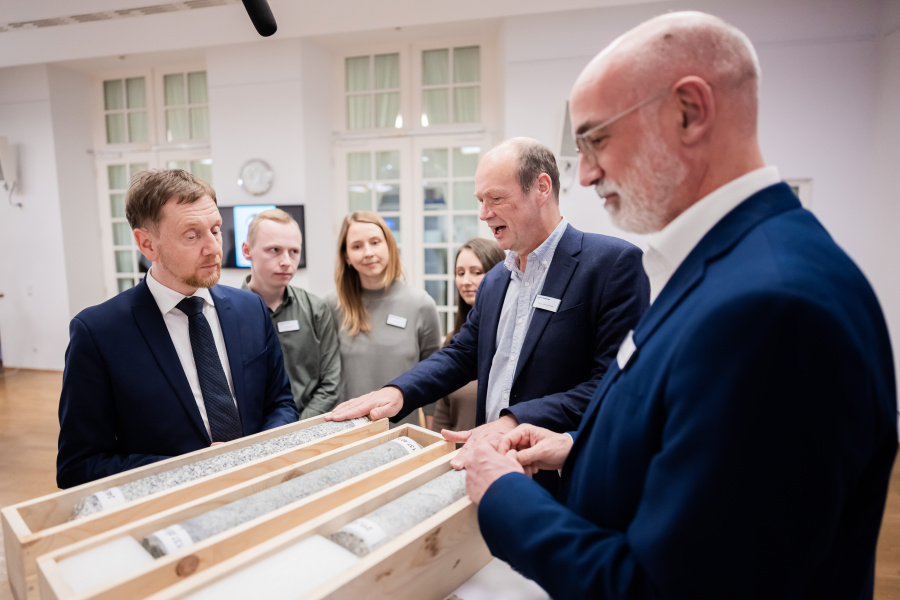 Gruppe von männlich und weiblich gelesenen Personen steht um einen Granitbohrkern.