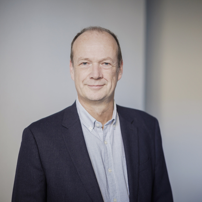 Männlich gelesene Person mit kurzen braunen Haaren blickt in die Kamera.