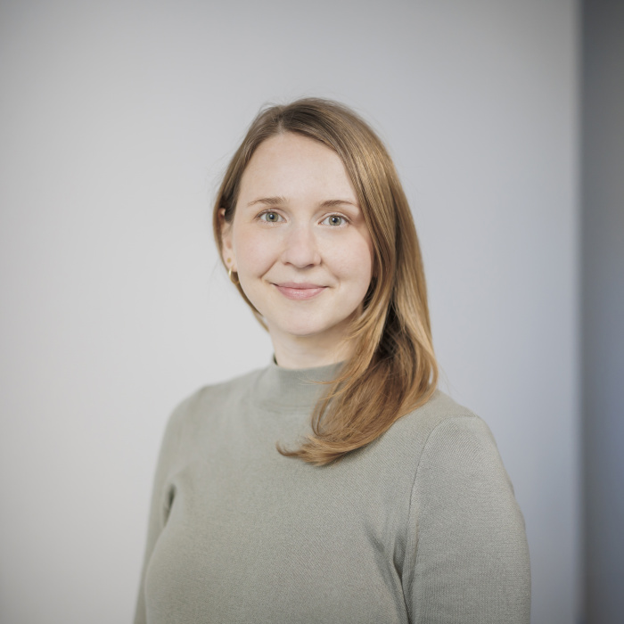 Weiblich gelesene Person mit langen Haaren blickt lächelnd in die Kamera.