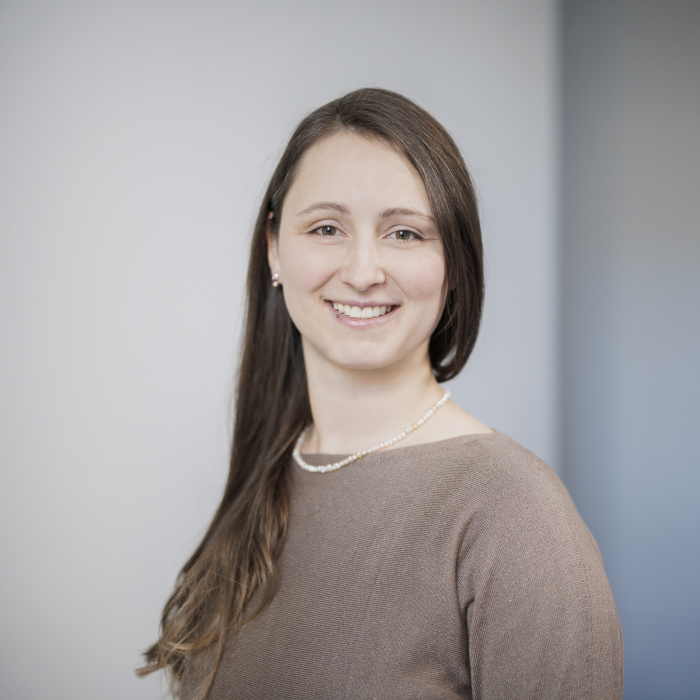 Weiblich gelesene Person mit braunen langen Haaren blickt lächelnd in die Kamera.